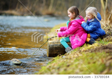Two cute little sisters playing with a stick by a river 33789164