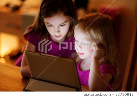 Two adorable little sisters playing with a digital tablet Two adorable little sisters playing with a digital tablet 33790912