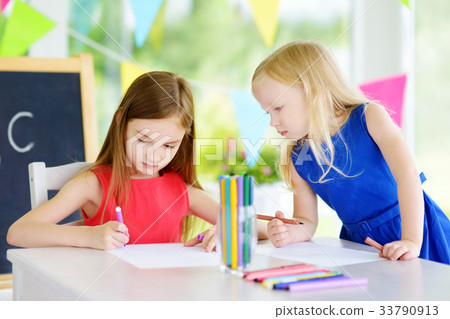 Two cute little sisters drawing with colorful pencils at a daycare Two cute little sisters drawing with colorful pencils at a daycare 33790913
