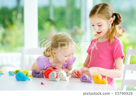 Two cute little sisters having fun together with colorful modeling clay at a daycare Two cute little sisters having fun together with colorful modeling clay at a daycare 33790926