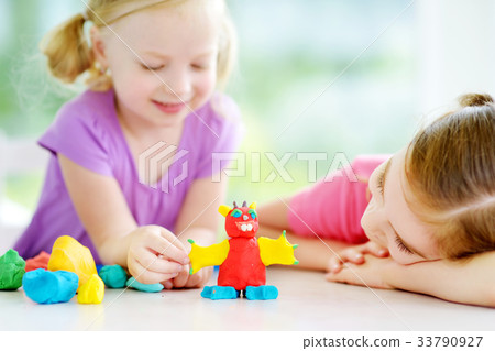 Two cute little sisters having fun together with colorful modeling clay at a daycare Two cute little sisters having fun together with colorful modeling clay at a daycare 33790927