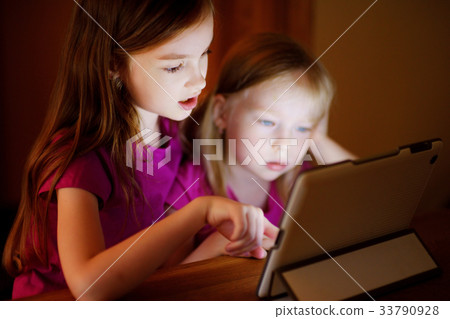 Two adorable little sisters playing with a digital tablet Two adorable little sisters playing with a digital tablet 33790928