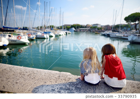 Two cute little sisters watching small yachts in harbor in Desenzano del Garda  33790935