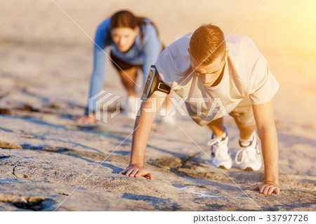 Young couple doing push ups on ocean beach 33797726