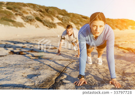 Young couple doing push ups on ocean beach 33797728