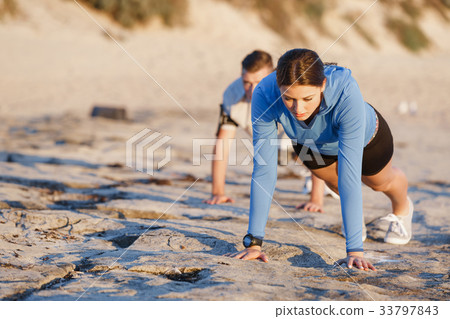 Young couple doing push ups on ocean beach 33797843