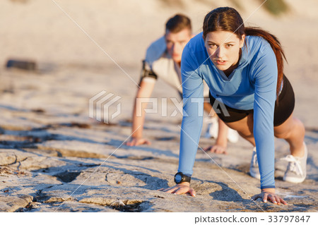 Young couple doing push ups on ocean beach Young couple doing push ups on ocean beach 33797847
