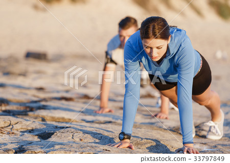 Young couple doing push ups on ocean beach 33797849