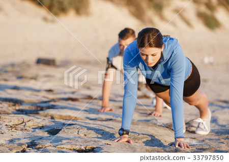 Young couple doing push ups on ocean beach Young couple doing push ups on ocean beach 33797850