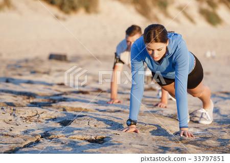 Young couple doing push ups on ocean beach Young couple doing push ups on ocean beach 33797851