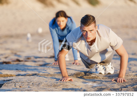 Young couple doing push ups on ocean beach Young couple doing push ups on ocean beach 33797852
