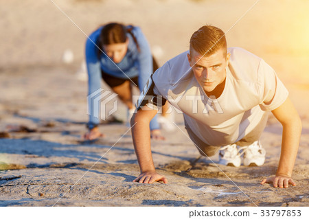 Young couple doing push ups on ocean beach 33797853