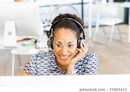 Portrait of smiling afro-american office worker sitting in offfice with headphones Portrait of smiling afro-american office worker sitting in offfice with headphones 33803413