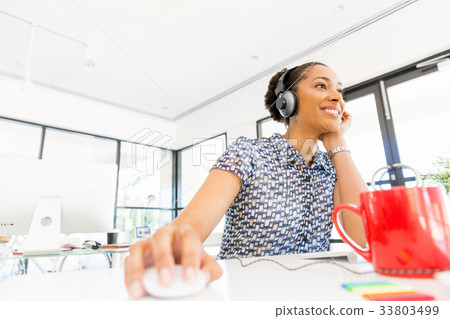 Portrait of smiling afro-american office worker sitting in offfice with headphones Portrait of smiling afro-american office worker sitting in offfice with headphones 33803499