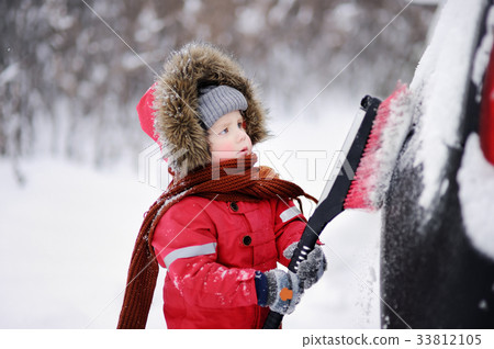 Cute little child helping to brush a snow from a car Cute little child helping to brush a snow from a car 33812105