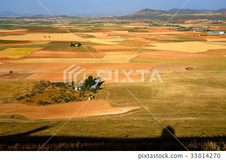 A patchworked rural landscape of La Mancha and a silhouette of a windmill 33814270