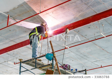 Worker welding red pipe hanging from the ceiling  33863788