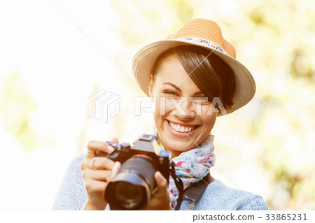 Outdoor summer smiling lifestyle portrait of pretty young woman with camera 33865231