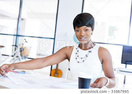 Young woman sitting at a desk in an office and working on blueprint Young woman sitting at a desk in an office and working on blueprint 33867995