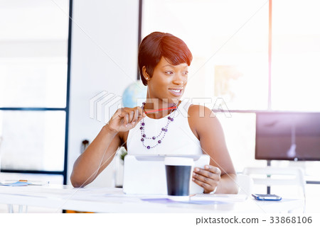 Young woman sitting at a desk in an office and working on blueprint Young woman sitting at a desk in an office and working on blueprint 33868106
