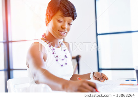 Young woman sitting at a desk in an office and working on blueprint Young woman sitting at a desk in an office and working on blueprint 33868264
