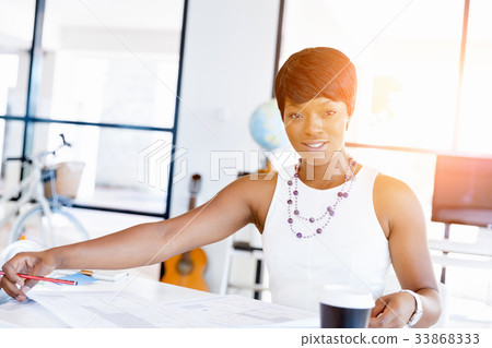 Young woman sitting at a desk in an office and working on blueprint 33868333