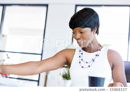 Young woman sitting at a desk in an office and working on blueprint Young woman sitting at a desk in an office and working on blueprint 33868337