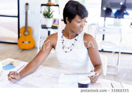 Young woman sitting at a desk in an office and working on blueprint 33868355