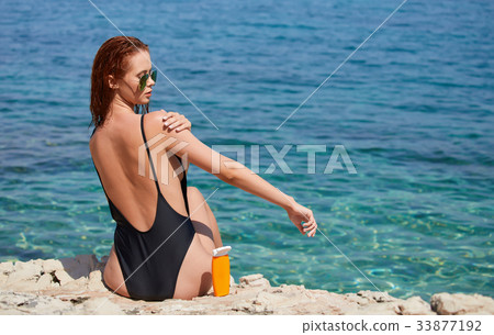 Girl in bikini applying sun lotion at seaside 33877192