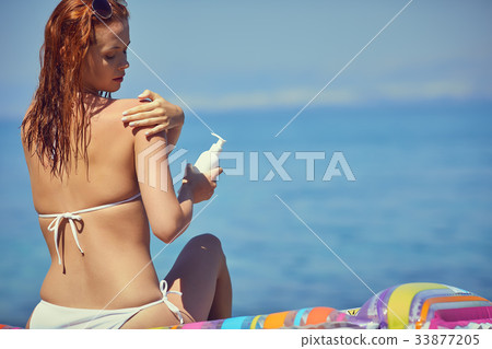 Girl in bikini applying sun lotion at seaside Girl in bikini applying sun lotion at seaside 33877205
