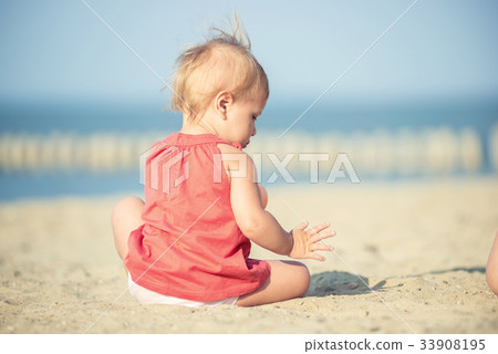 Baby girl in red dress playing on sandy beach near Baby girl in red dress playing on sandy beach near 33908195