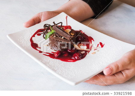 Customer holds chocolate cake with cherry jam Customer holds chocolate cake with cherry jam 33921598