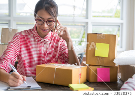start up small business owner talking with customer on mobile phone at her shop. freelance woman entrepreneur SME seller writing product order. Online selling, internet marketing, e-commerce concept 33928375