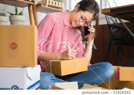start up small business owner talking with customer on mobile phone at her shop. freelance woman entrepreneur SME seller writing address on parcel box. Online selling, internet marketing, e-commerce concept 33928385