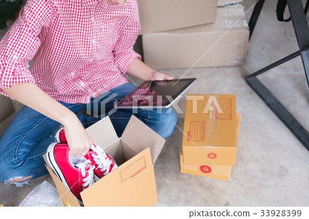 start up small business owner packing shoes in the box at workplace. freelance woman entrepreneur SME seller prepare product for packaging process while checking order with tablet at home. Online selling, internet marketing, e-commerce concept 33928399