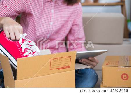 start up small business owner packing shoes in the box at workplace. freelance woman entrepreneur SME seller prepare product for packaging process while checking order with tablet at home. Online selling, internet marketing, e-commerce concept start up small business owner packing shoes in the box at workplace. freelance woman entrepreneur SME seller prepare product for packaging process while checking order with tablet at home. Online selling, internet marketing, e-commerce concept 33928416