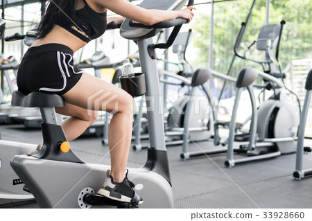 young woman execute exercise in fitness center. female athlete riding stationary bicycle in gym. sporty girl working out in health club. 33928660