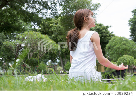 Yoga outdoors in public park. Asian woman sits in lotus position. Young female with zen gesturing. healthy lifestyle and relaxation concept 33929284