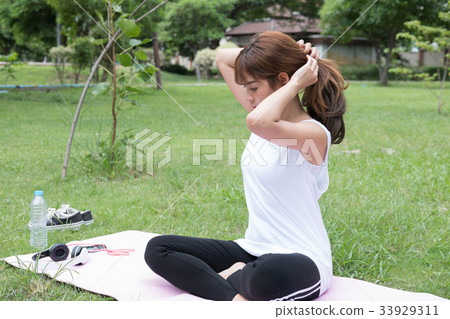 young asian woman ties her hair in a ponytail while sitting in public park 33929311