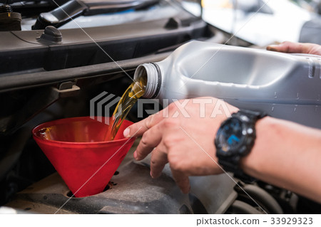 mechanic pouring oil to vehicle engine. serviceman changing motor oil in automobile repair service. maintenance & checkup in car workshop. 33929323