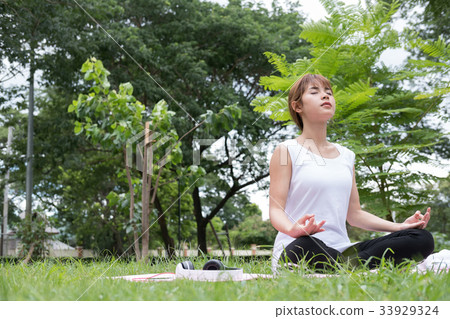 Yoga outdoors in public park. Asian woman sits in lotus position. Young female with zen gesturing. healthy lifestyle and relaxation concept 33929324