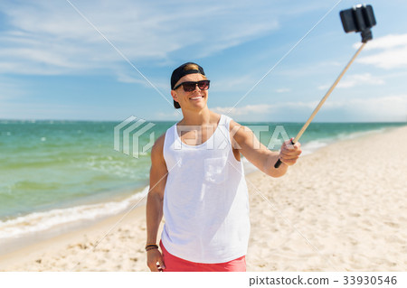 man with smartphone selfie stick on summer beach 33930546