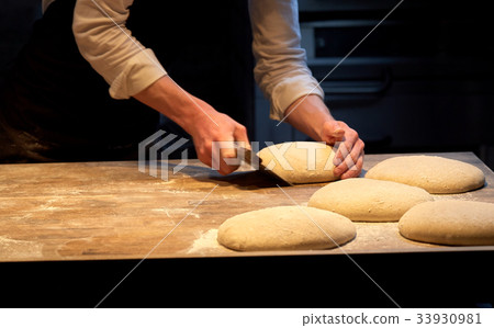 baker portioning dough with bench cutter at bakery 33930981