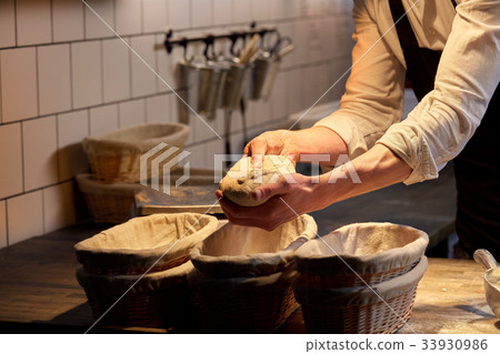 baker with dough rising in baskets at bakery 33930986