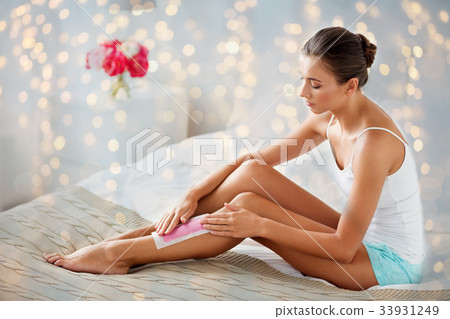 woman epilating leg hair with wax strip at home 33931249