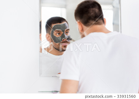 young man applying clay mask to face at bathroom young man applying clay mask to face at bathroom 33931560