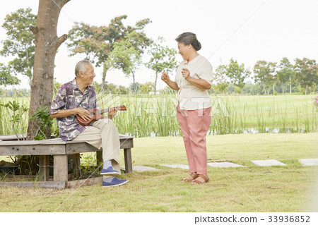 A picture of an elderly couple playing guitar and dancing in a park 33936852