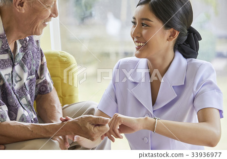 a smiling nurse is touching senior man's hand to check pulse 33936977