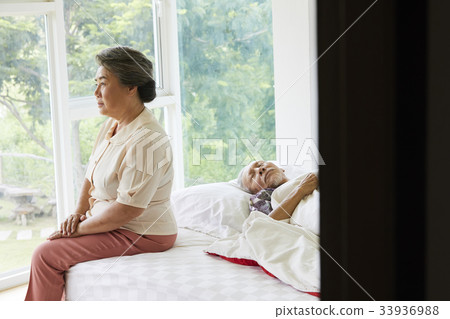 A senior woman is sitting and a senior man is lying on the bed 33936988