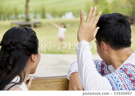 A married couple is looking at their daughter and waving in the park 33936997